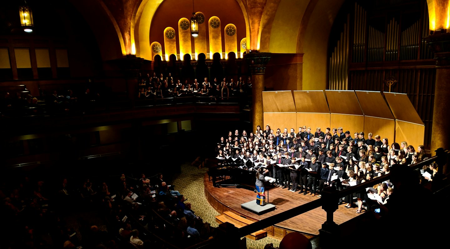 Coro actuando en el escenario de un gran auditorio.