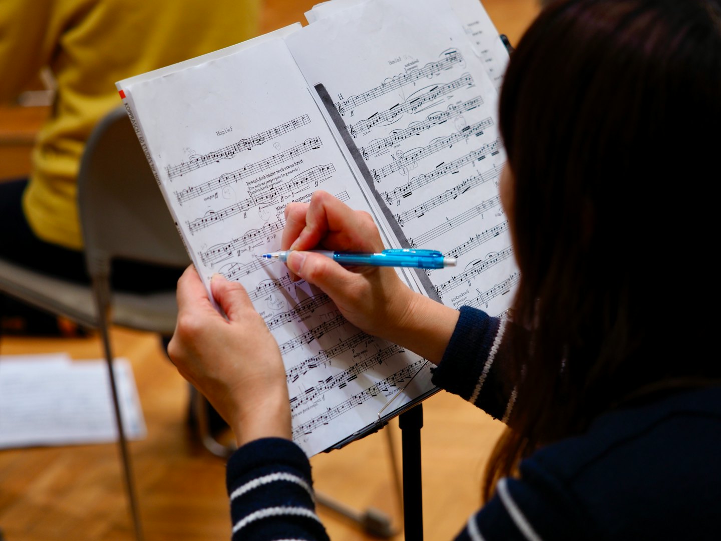 Manos escriben notas en una partitura con un bolígrafo azul.